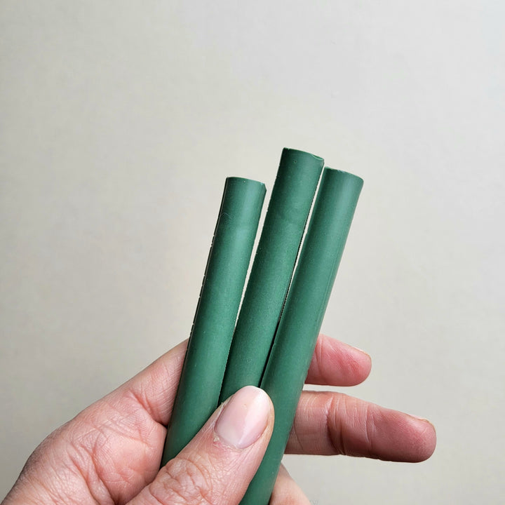 Hand holding three heritage green 11mm sealing wax sticks from a pack of 10, ideal for arts and crafts projects or decorative sealing.