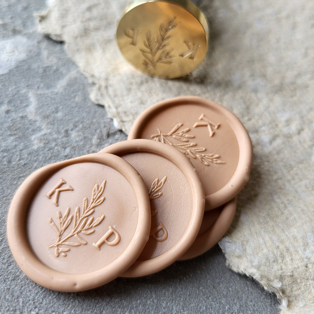 Close-up of peach 'Willow' monogram wax seals with initials 'K' and 'P,' showcasing the brass stamp and detailed botanical design.