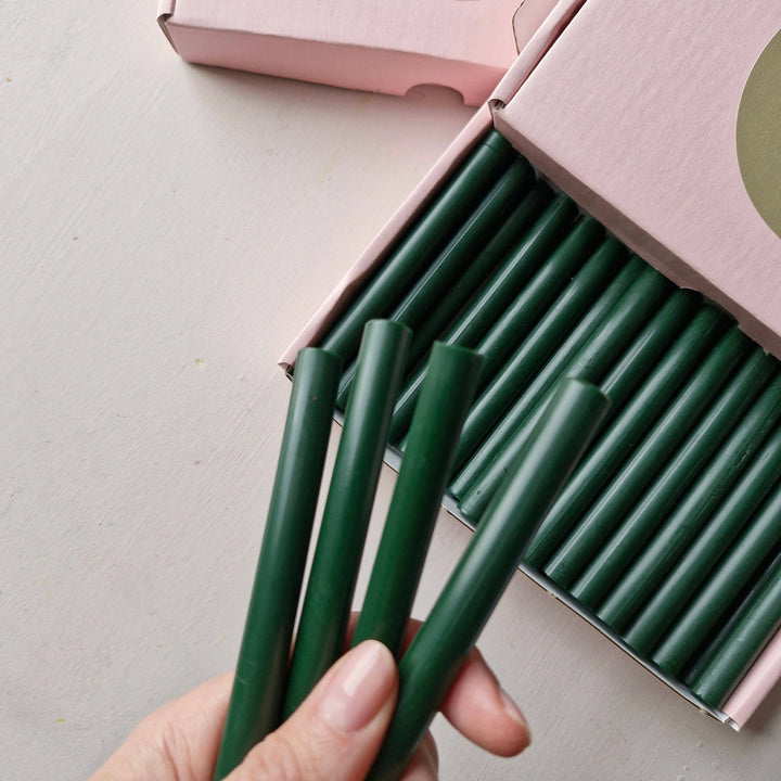 Hand holding 11mm British Racing Green sealing wax sticks from a box of 30, ideal for crafting and sealing projects.