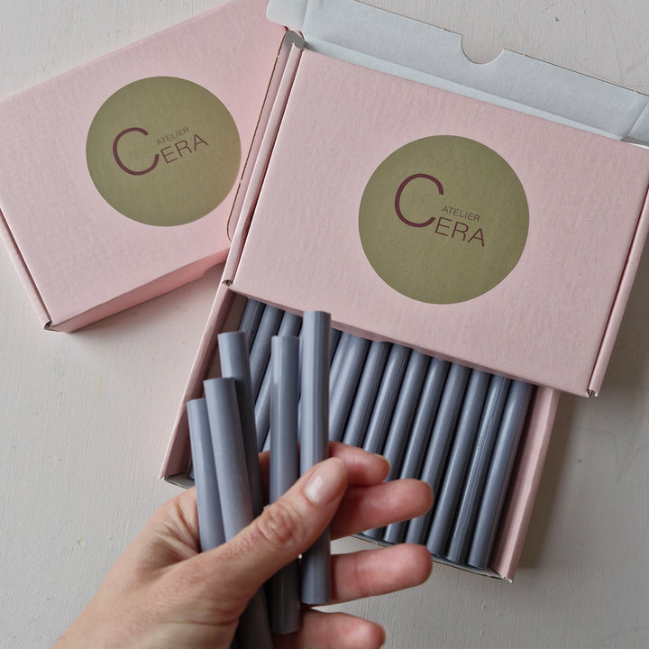 Box of 30 - 11mm Lavender Blue office instruments in a pink Atelier Cera branded box, with a hand holding several pieces.