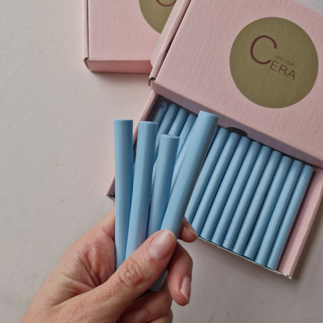 Hand holding several 11mm dusty blue sealing wax sticks from a box of 30, ideal for crafting and office use.