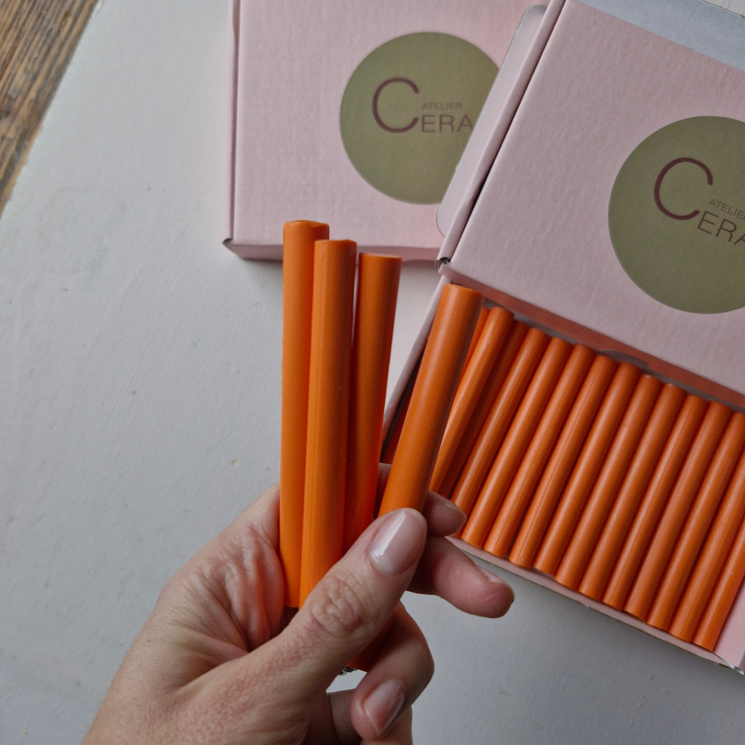 Hand holding vibrant 11mm tangerine sealing wax sticks from a box of 30. Perfect for crafts, envelopes, and handmade projects.