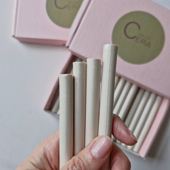 Close-up of hand holding 11mm champagne pearl sealing wax sticks with pink 'Atelier Cera' box in the background. Perfect for handmade seals.