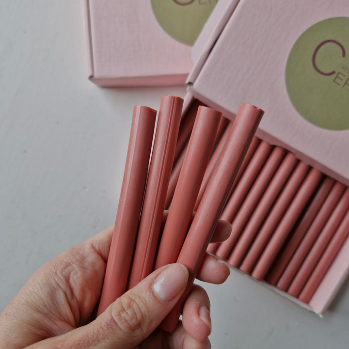 Hand holding 11mm antique pink sealing wax sticks from a box of 30, showcasing their smooth finish and handmade quality.