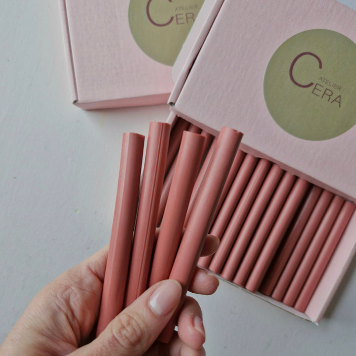 Four antique pink sealing wax sticks held in hand, with a box of 30 in the background, showcasing their handmade design.