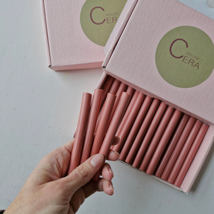 Hand displaying several antique pink sealing wax sticks with an open box of 30 in the background, ideal for sealing needs.