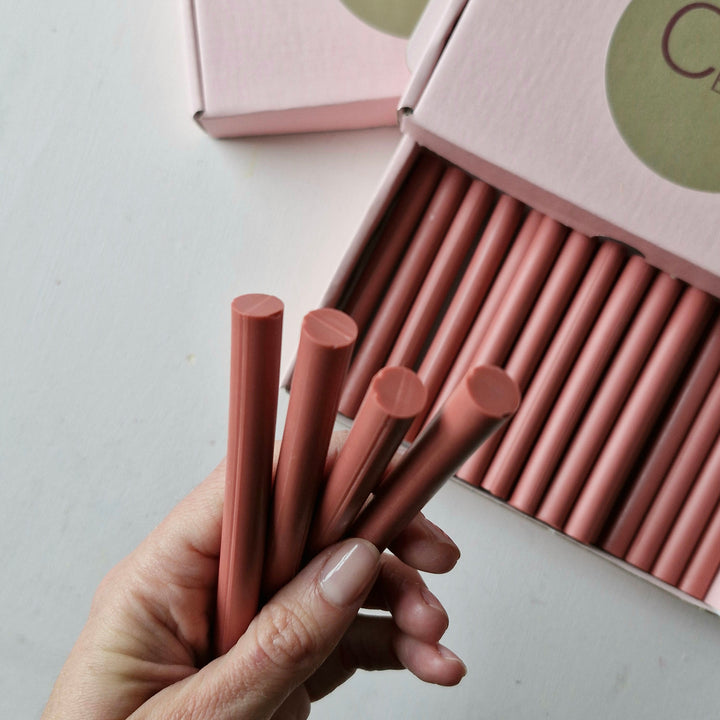 Close-up of a hand holding four 11mm antique pink sealing wax sticks, emphasizing their cylindrical shape and polished texture.