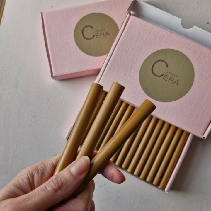 Hand displaying three 11mm toffee sealing wax sticks in front of an open pink box containing 30 handmade sticks. Ideal for crafts and sealing.