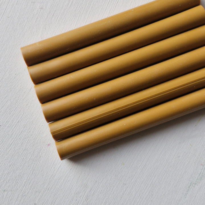 Close-up of 11mm toffee-colored sealing wax sticks arranged on a white surface. Ideal for crafting and sealing projects, box of 50.