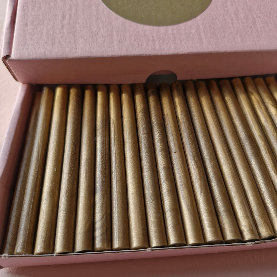 Close-up view of gold 7mm sealing wax sticks with handmade texture, neatly arranged in a pink box labeled 'Atelier Cera.'