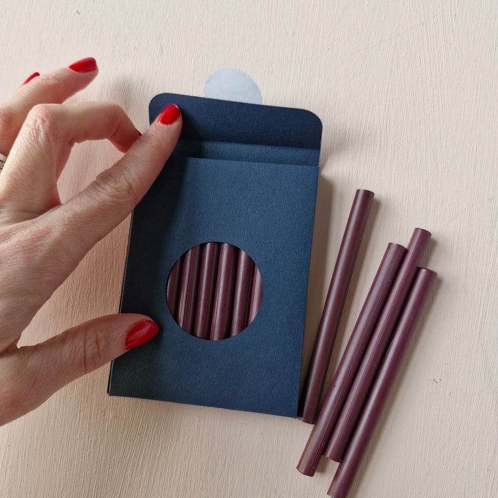 Pack of 10 burgundy 7mm sealing wax sticks in a navy blue box with a circular window. Ideal for creating up to 50 wax seals for envelopes and invitations.