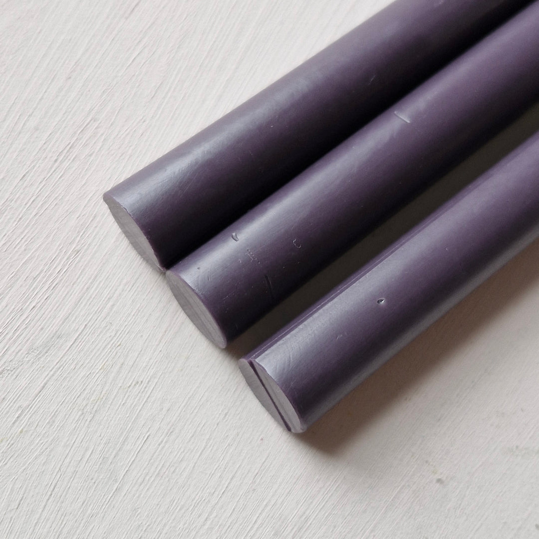 Close-up of three plum sealing wax sticks on a white surface. Smooth 11mm design suitable for elegant sealing needs.