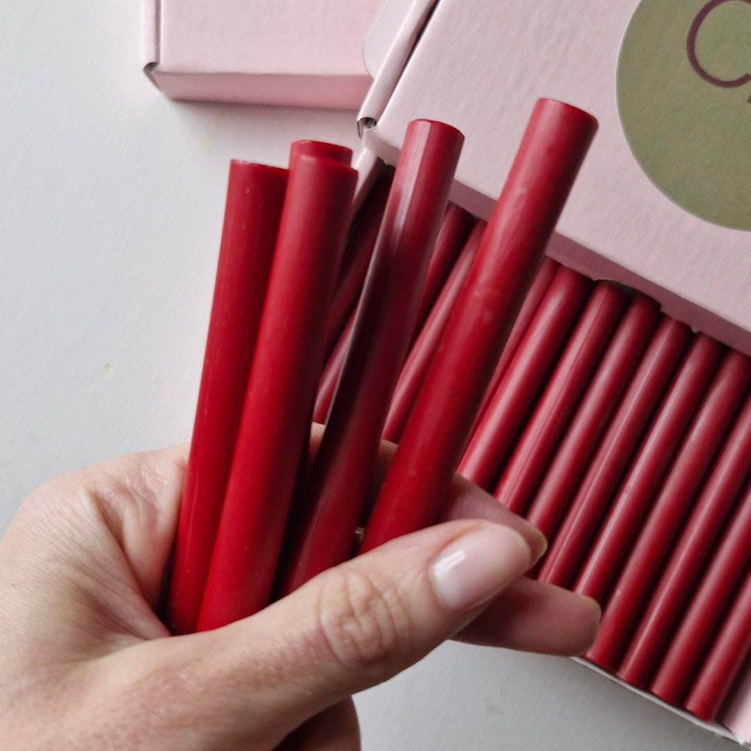 Hand holding multiple 11mm red wax sticks from a box of 30, ideal for sealing and crafting purposes.