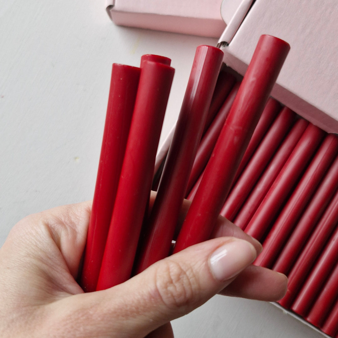 Hand displaying several red wax sticks from a box of 30, highlighting their 11mm diameter and quality finish.