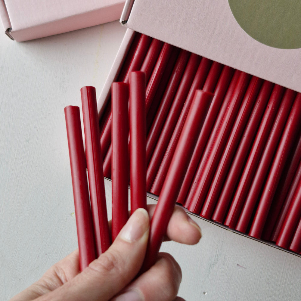 Hand holding several classic red 7mm sealing wax sticks from a box of 60, perfect for crafting and sealing tasks.