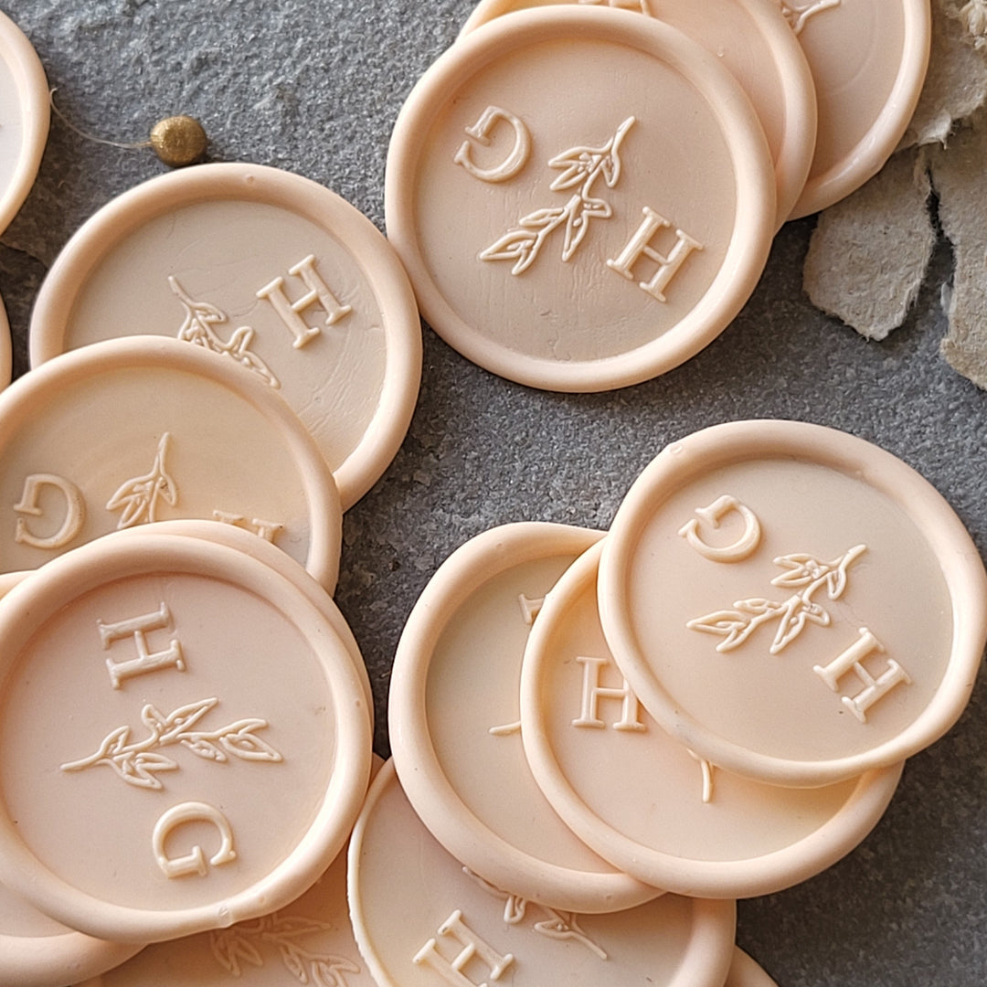 Customizable 'Meadow' monogram wax seals in beige with initials and leaf design, ideal for envelopes and stationery.