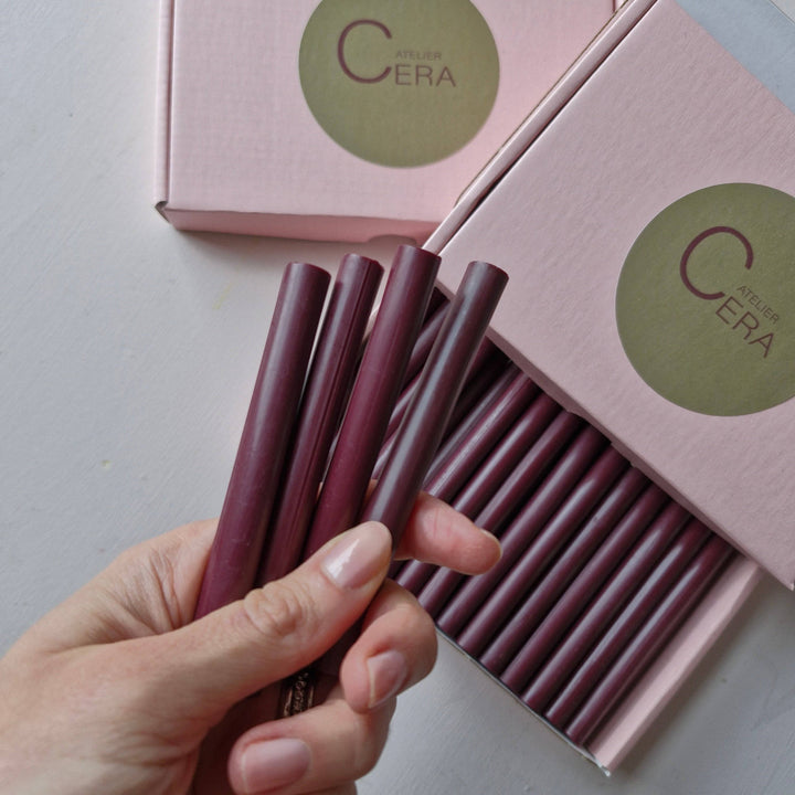 Hand holding burgundy 11mm wax sticks from a box of 30, packaged in pink boxes with Atelier Cera branding. Ideal for office use.