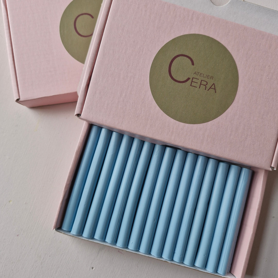 Close-up of a box containing 100 dusty blue 11mm sealing wax sticks, neatly arranged in a pink box with a gold Atelier Cera logo.