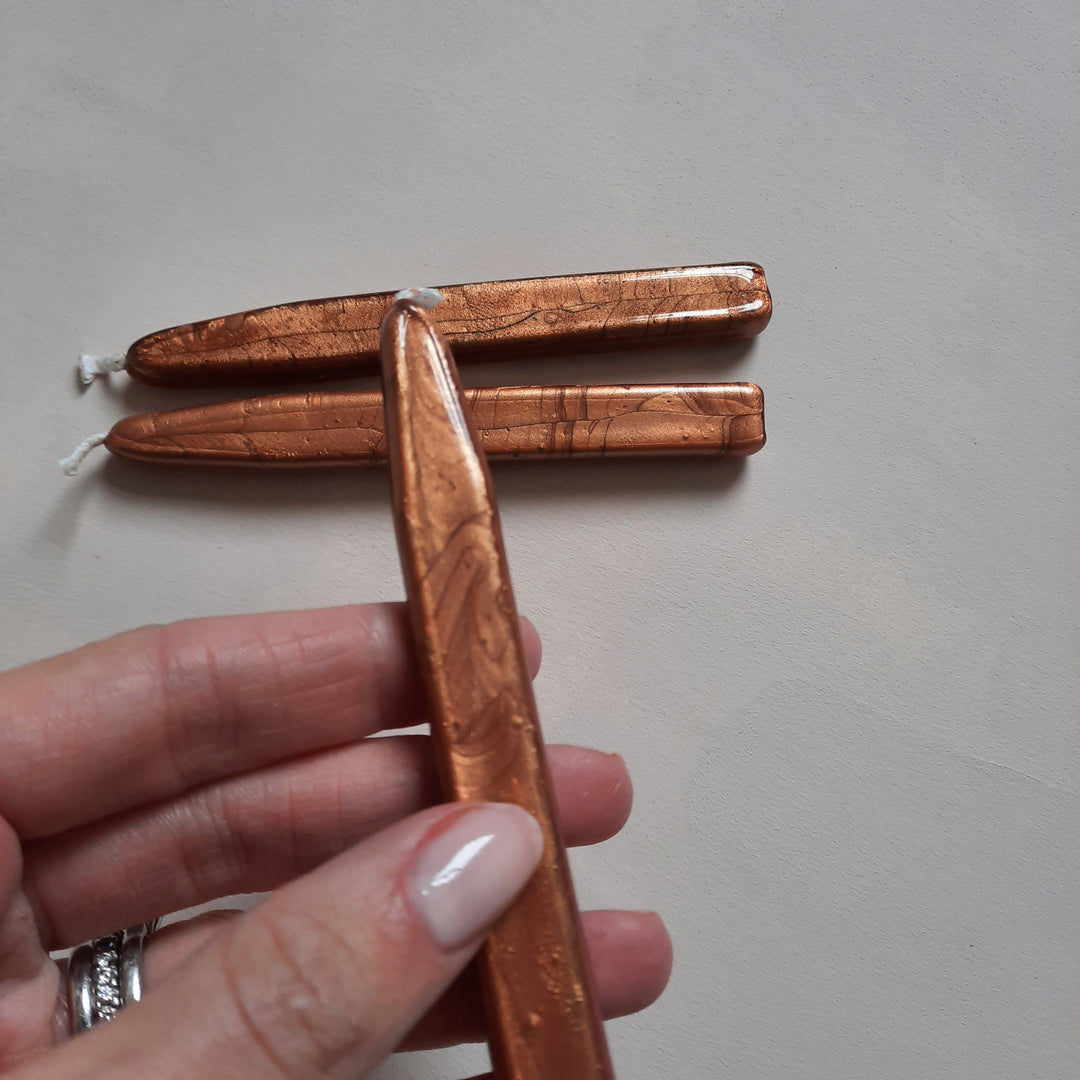 Hand holding a Copper Sealing Wick Wax stick with two additional wax sticks placed on a light surface. Traditional handcrafted design.